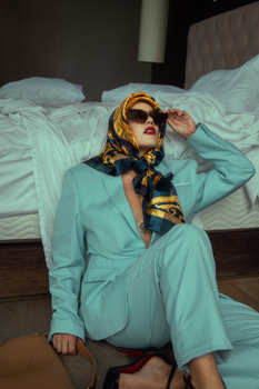 Sophisticated woman in a fashionable suit and scarf posing in a hotel room.