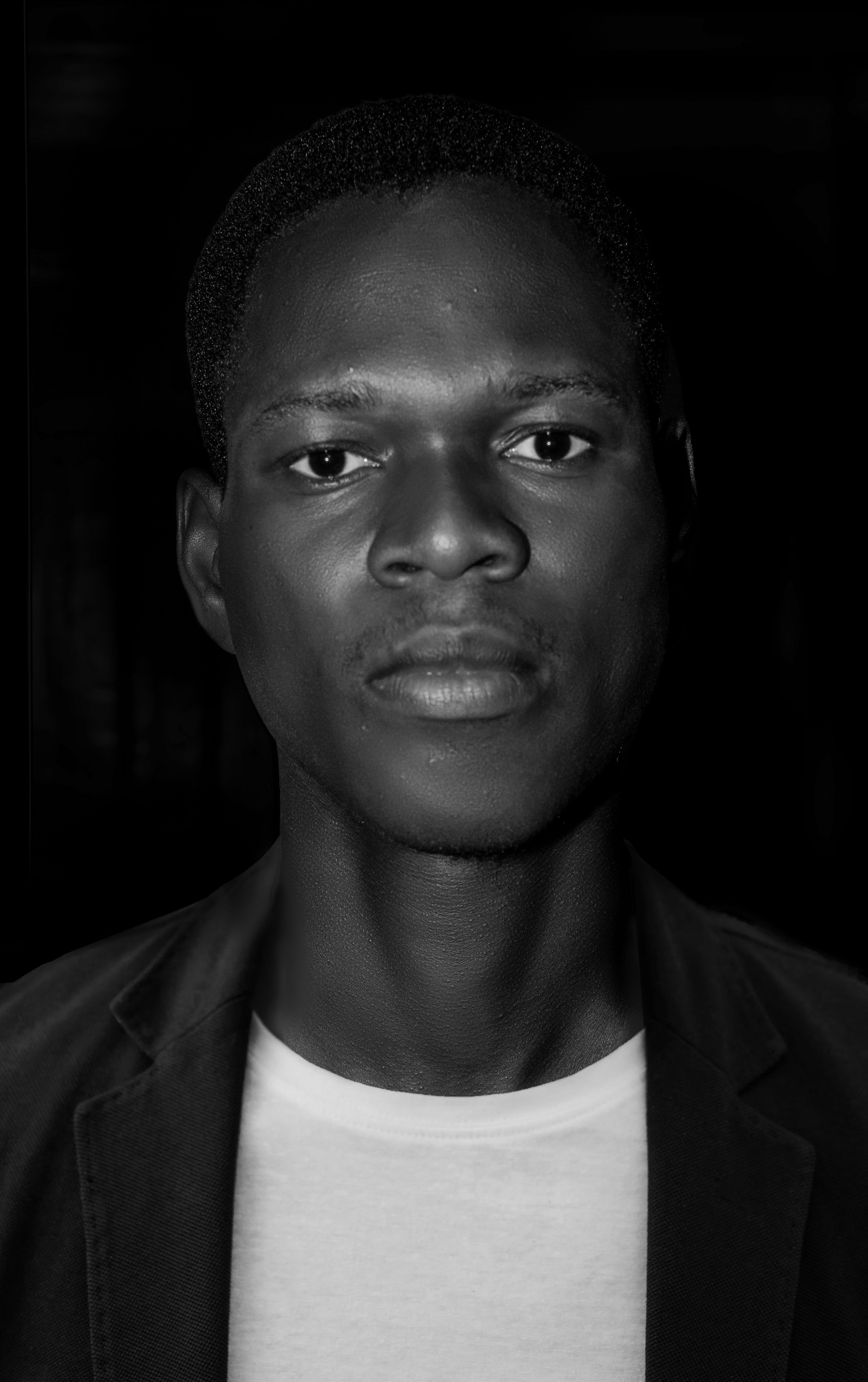 Striking black and white portrait of a young man with a serious expression, captured in a studio setting.