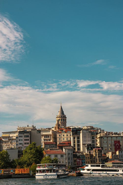 Free Scenic view of Galata Tower surrounded by city buildings and boats on a sunny day. Stock Photo