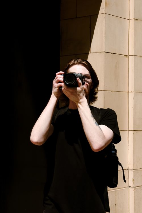 Free Adult male photographer captures moments in an urban setting, highlighting shadow play. Stock Photo