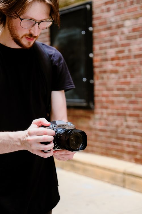 Free Young male photographer reviewing images on a retro-style camera in a vibrant urban setting. Stock Photo