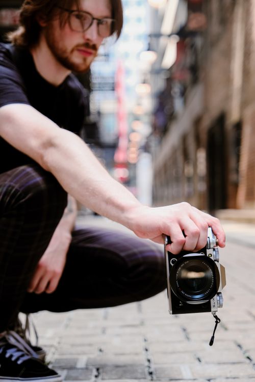 Free Stylish urban portrait capturing a young photographer with a camera in an alleyway. Stock Photo