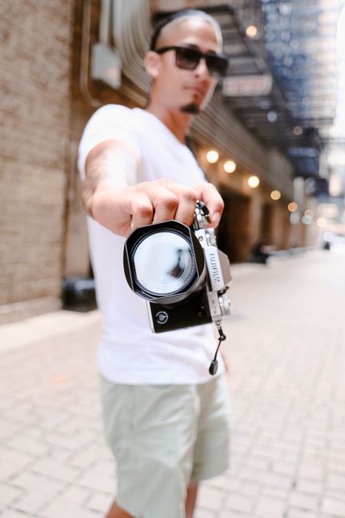 Free Stylish young man holding a camera in a vibrant urban alleyway, showcasing modern photography. Stock Photo