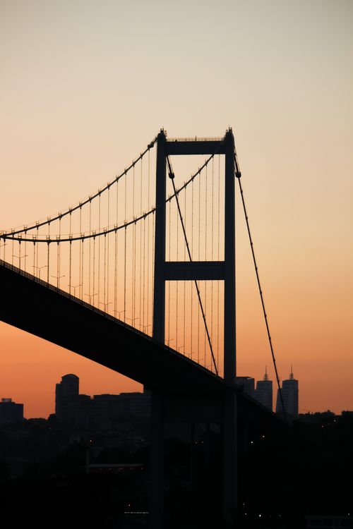Free A stunning silhouette of a suspension bridge against a vibrant sunset sky. Stock Photo