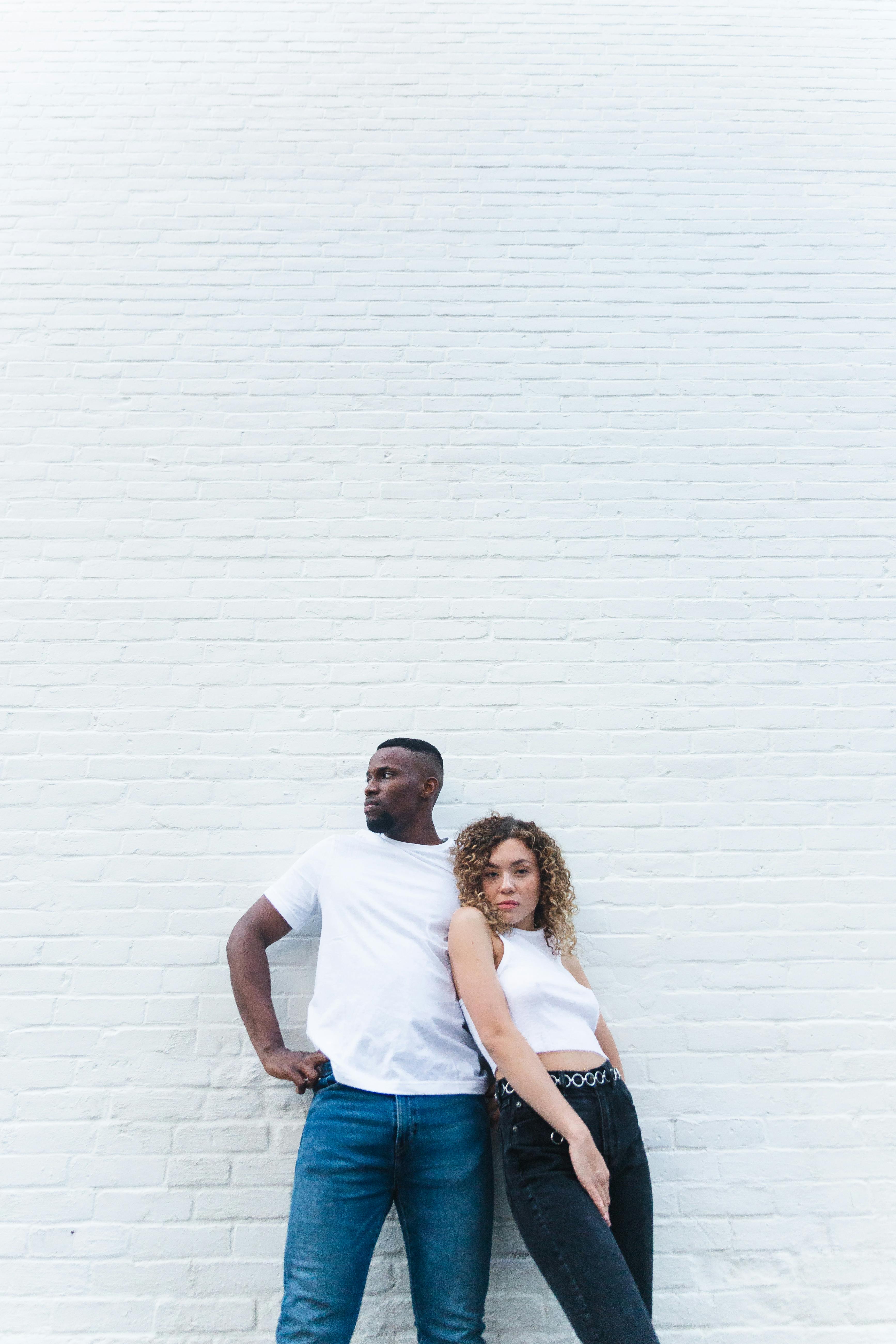 man and woman wearing white top while standing near wall