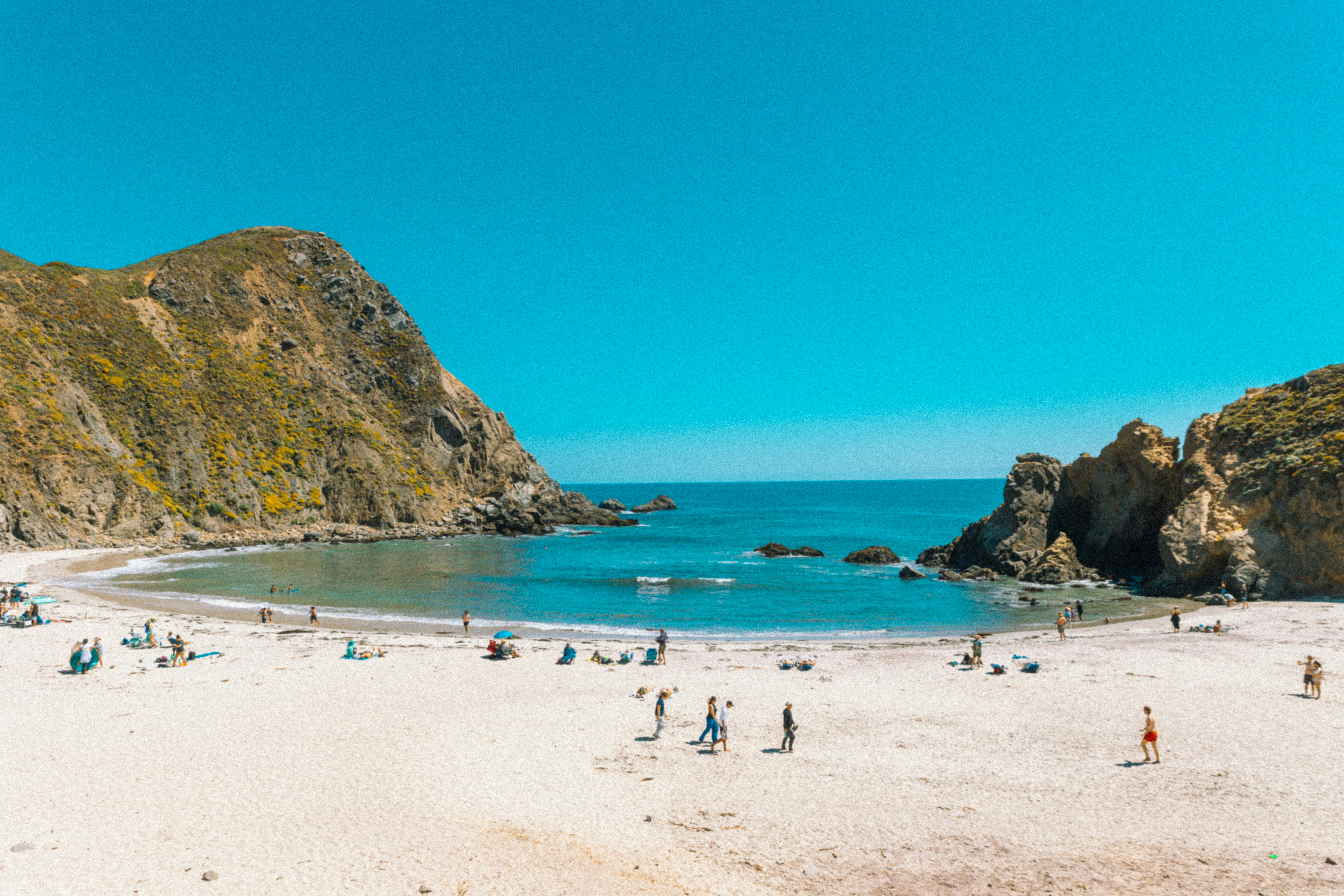 A vibrant beach scene at Big Sur, CA with clear blue waters and people enjoying the sun.