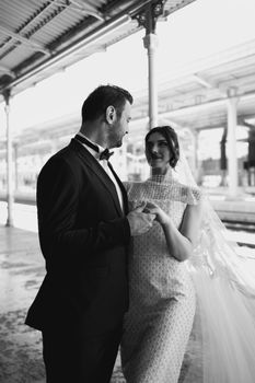 A timeless black and white portrait of a couple in wedding attire sharing a moment at a train station.