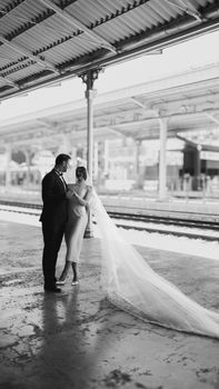 Elegant black and white portrait of a bride and groom at a train station, showcasing their love.