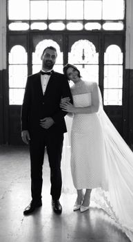 Black and white portrait of a bride and groom standing indoors, exuding elegance