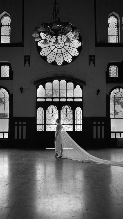 Free A bride stands gracefully in a historic hall with stunning stained glass windows, exuding timeless elegance. Stock Photo