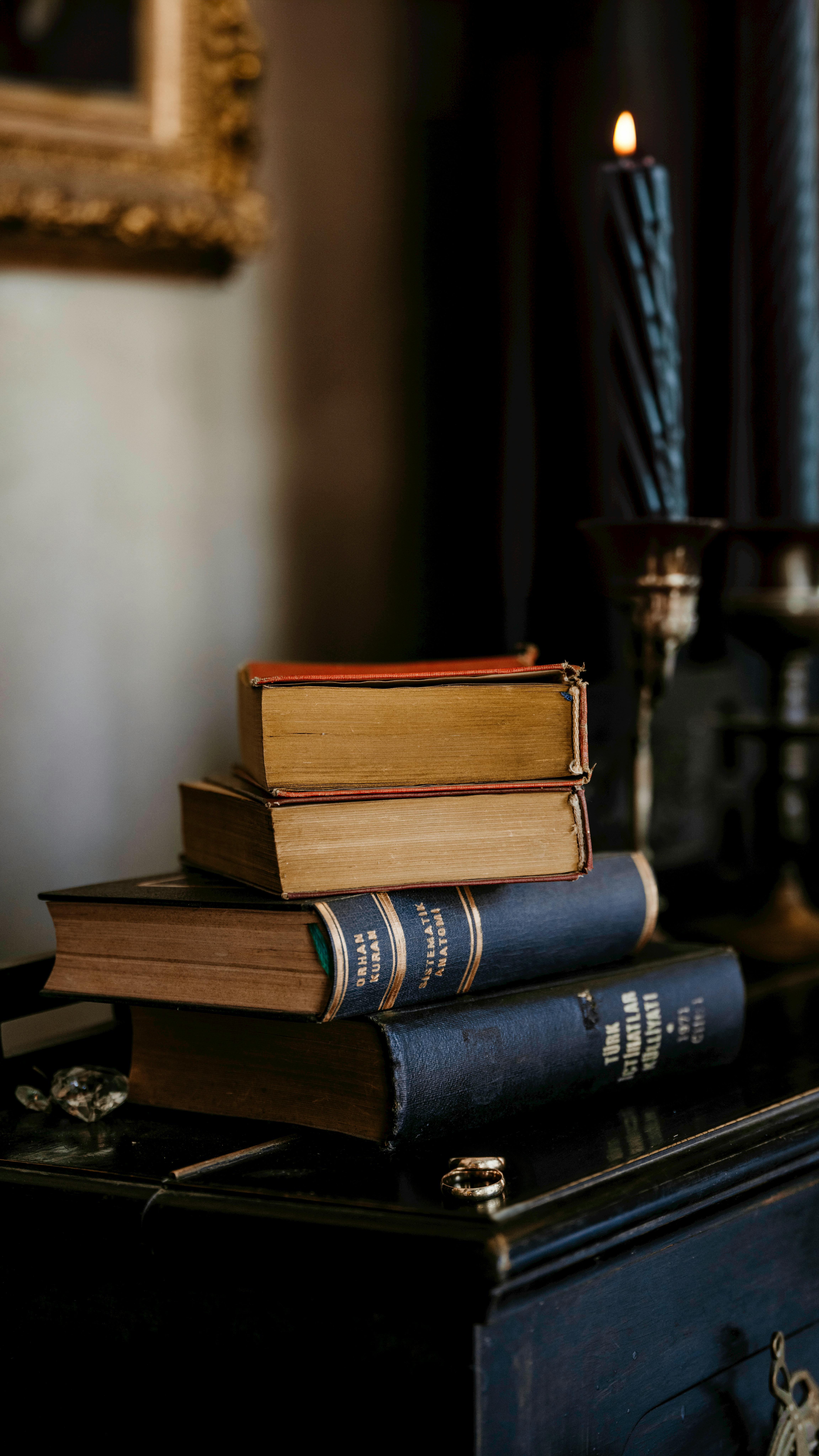 Stack of vintage books beside lit candle, evoking a classic, mysterious atmosphere.