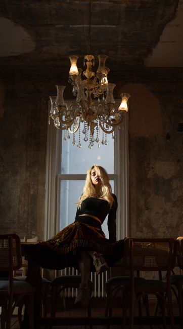 A stylish woman in an elegant room with a chandelier, exuding classic fashion vibes.