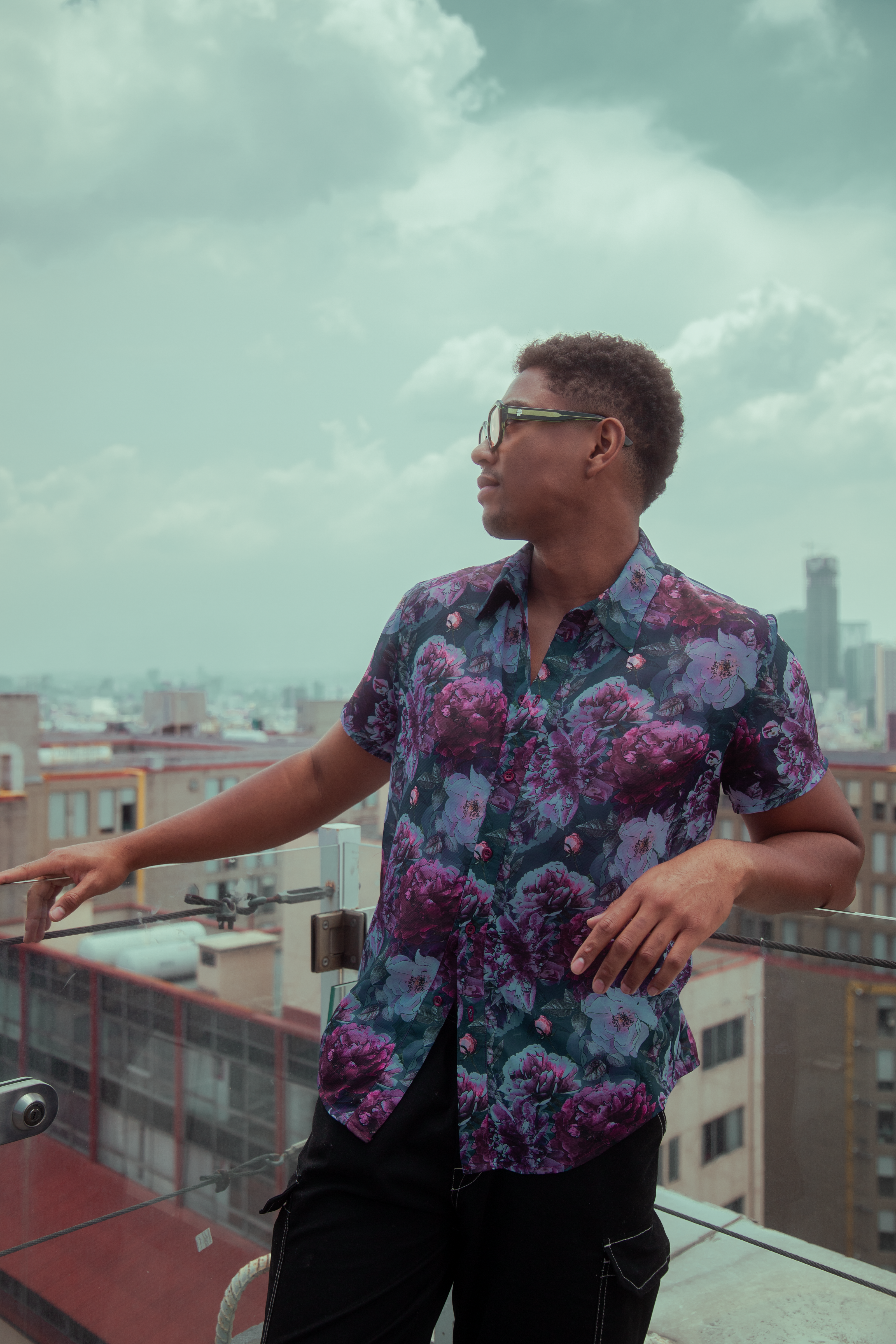 Homem com camisa floral apreciando a vista urbana do terraço na Cidade do México.