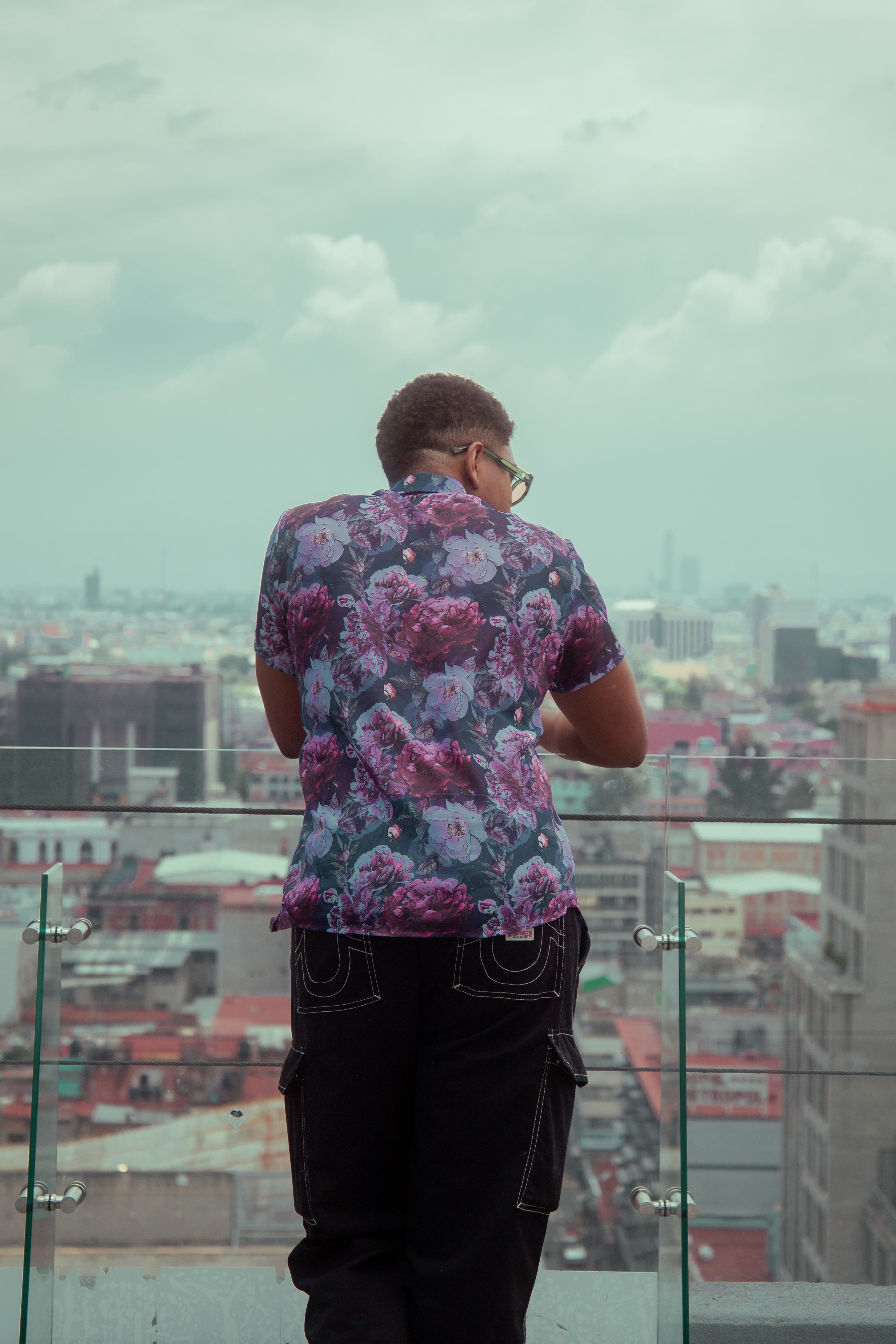 Adulto estiloso em camisa floral contemplando a Cidade do México de um telhado, abraçando a moda urbana.