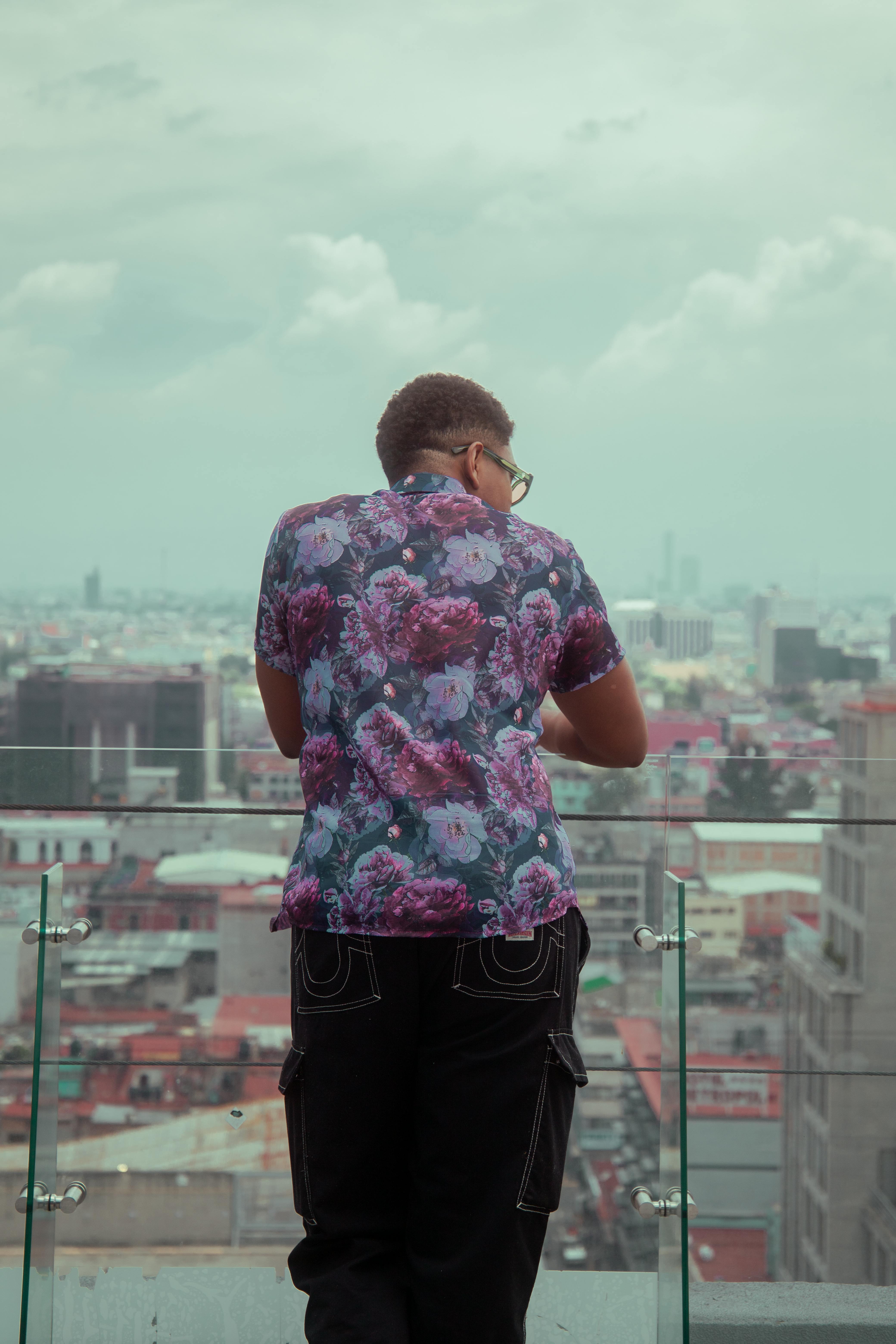 Free Stylish adult male in floral shirt gazing over Mexico City from rooftop, embracing urban fashion. Stock Photo
