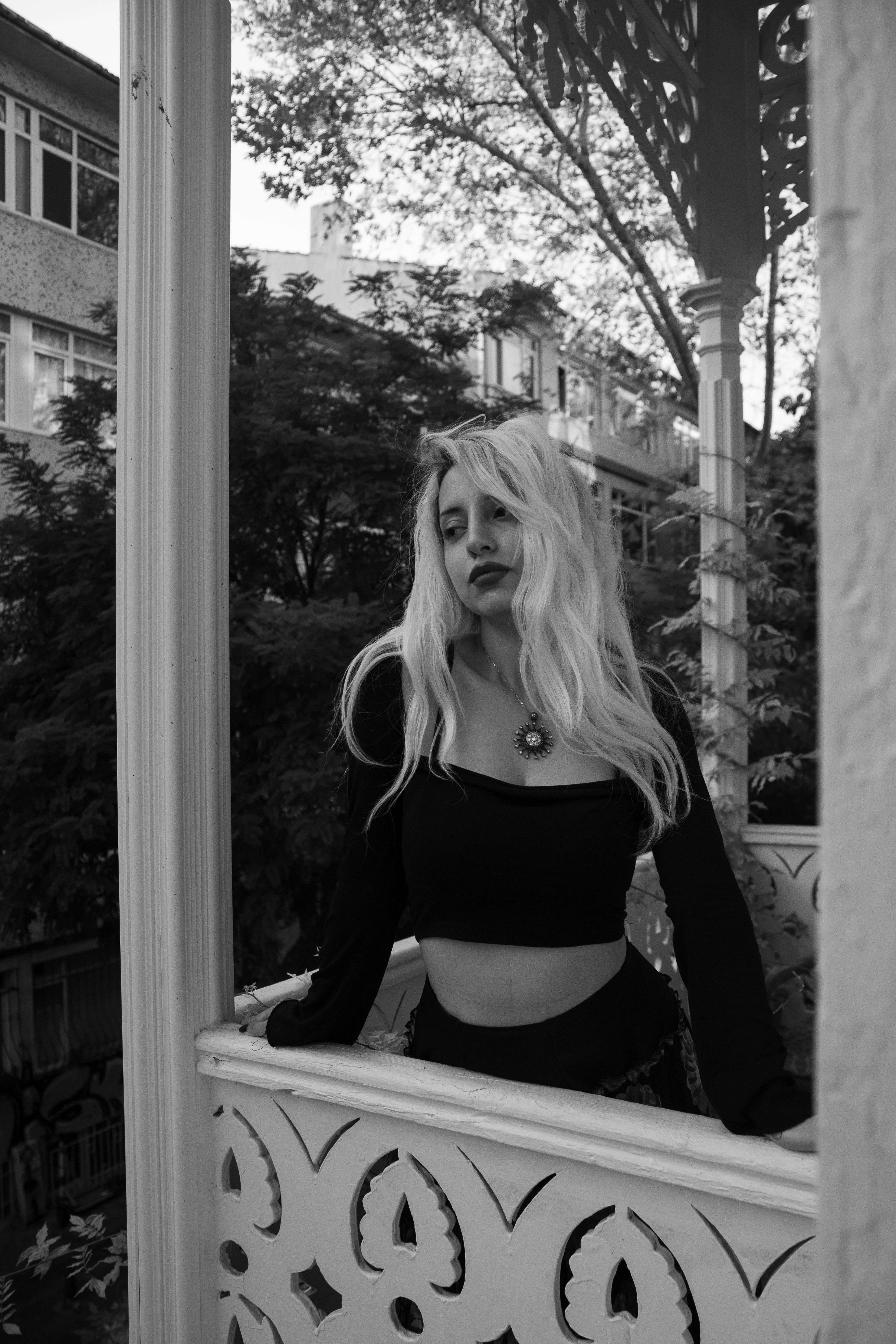 Monochrome portrait of a stylish woman standing on a decorative balcony, highlighting fashion and elegance.