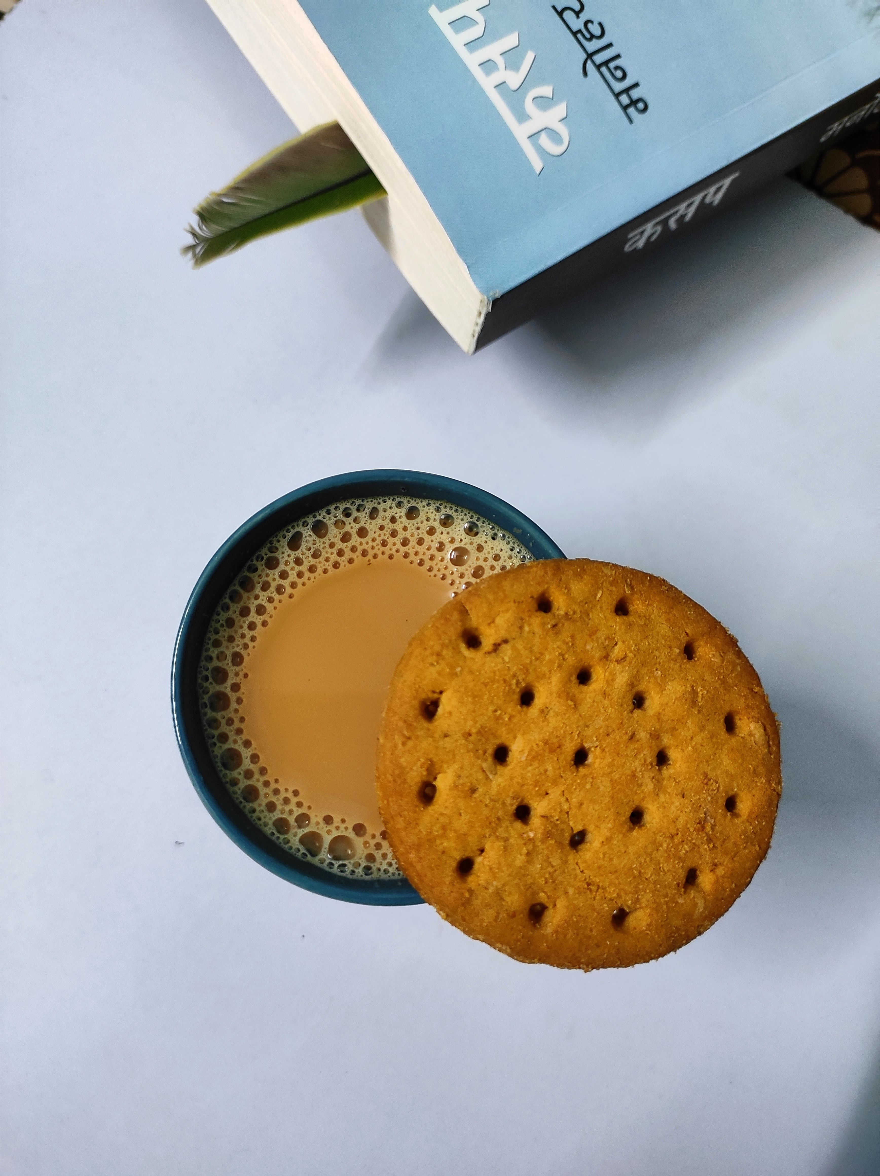 A cozy setup with a cup of chai and a biscuit next to an open book, perfect for relaxation moments.