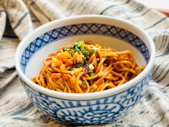 Wheat noodles glossy with red chili sesame sauce and scallions in a blue bowl