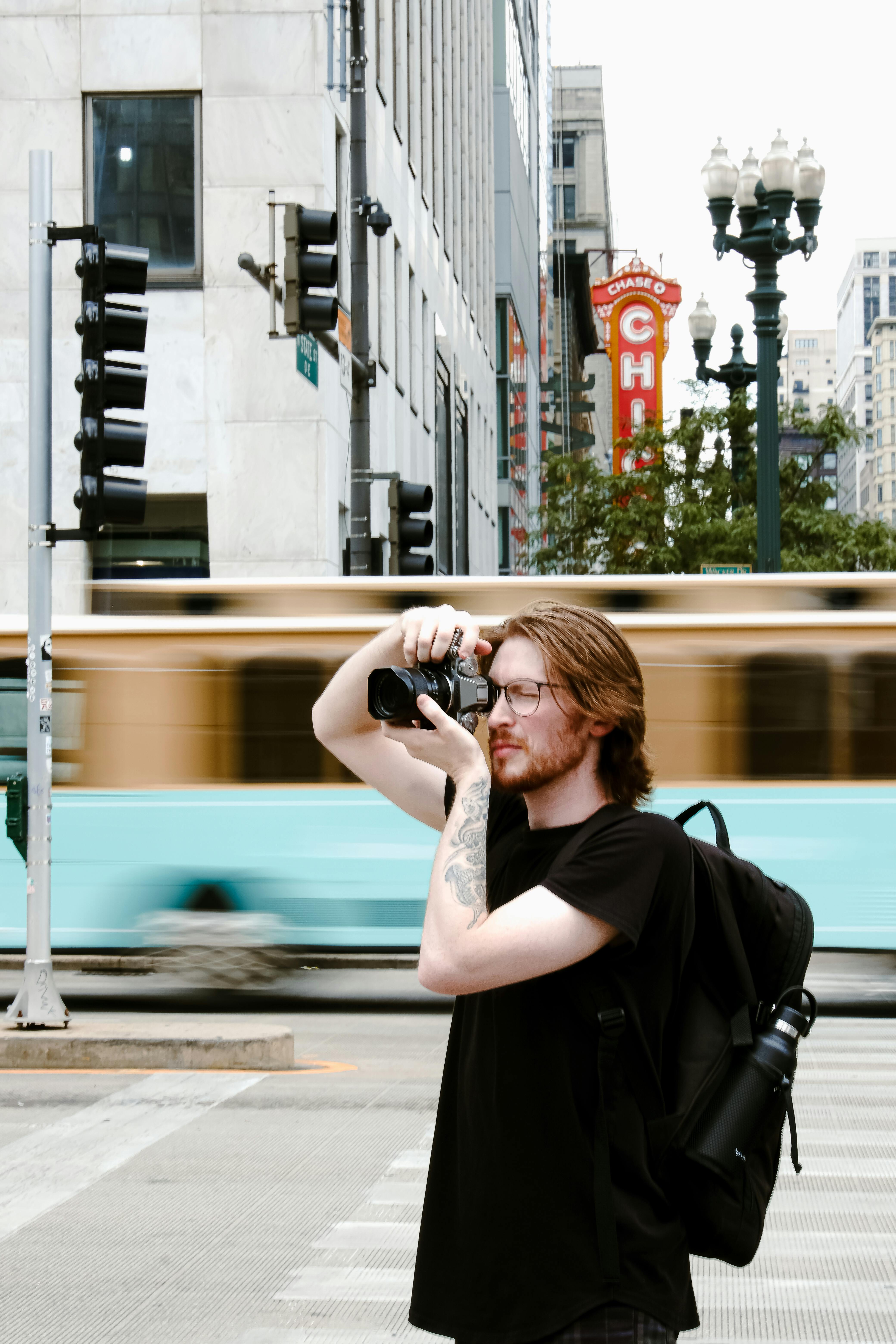 Photographer taking a picture in bustling city with blurred traffic background.