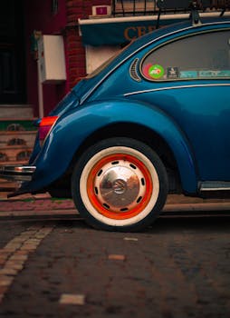 Classic blue Volkswagen Beetle parked on a cobblestone street in urban setting.