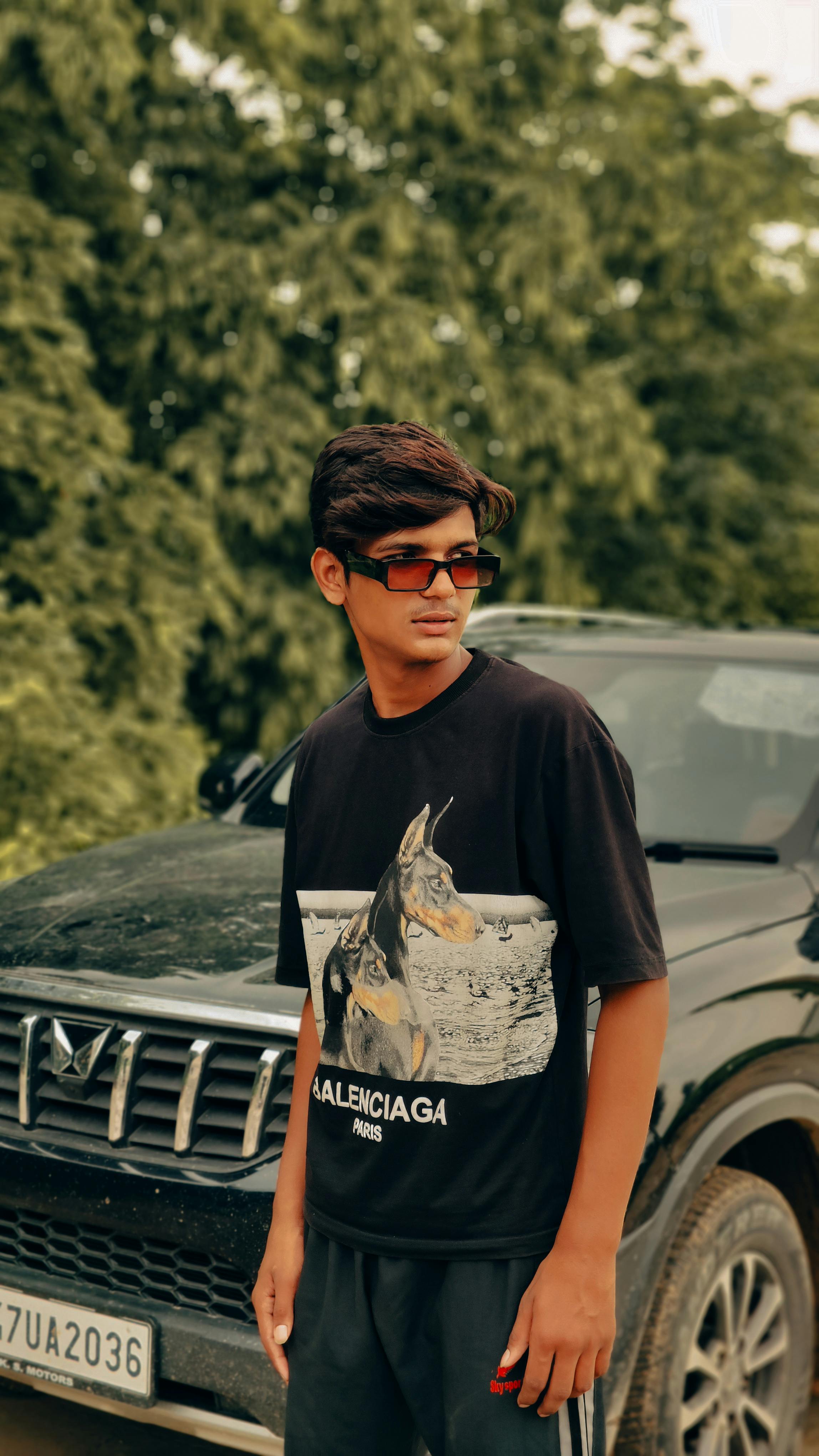 Teenager posing with car wearing sunglasses and fashion t-shirt, captured outdoors in summer.