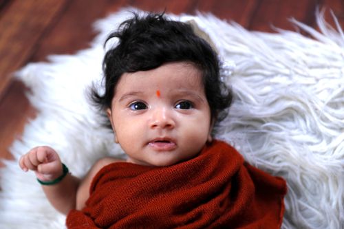 Free Portrait of a cute baby wrapped in a red blanket on a fluffy surface indoors. Stock Photo