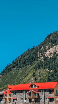 Scenic view of a mountain lodge with a vibrant red roof set against lush green hills under a clear blue sky.