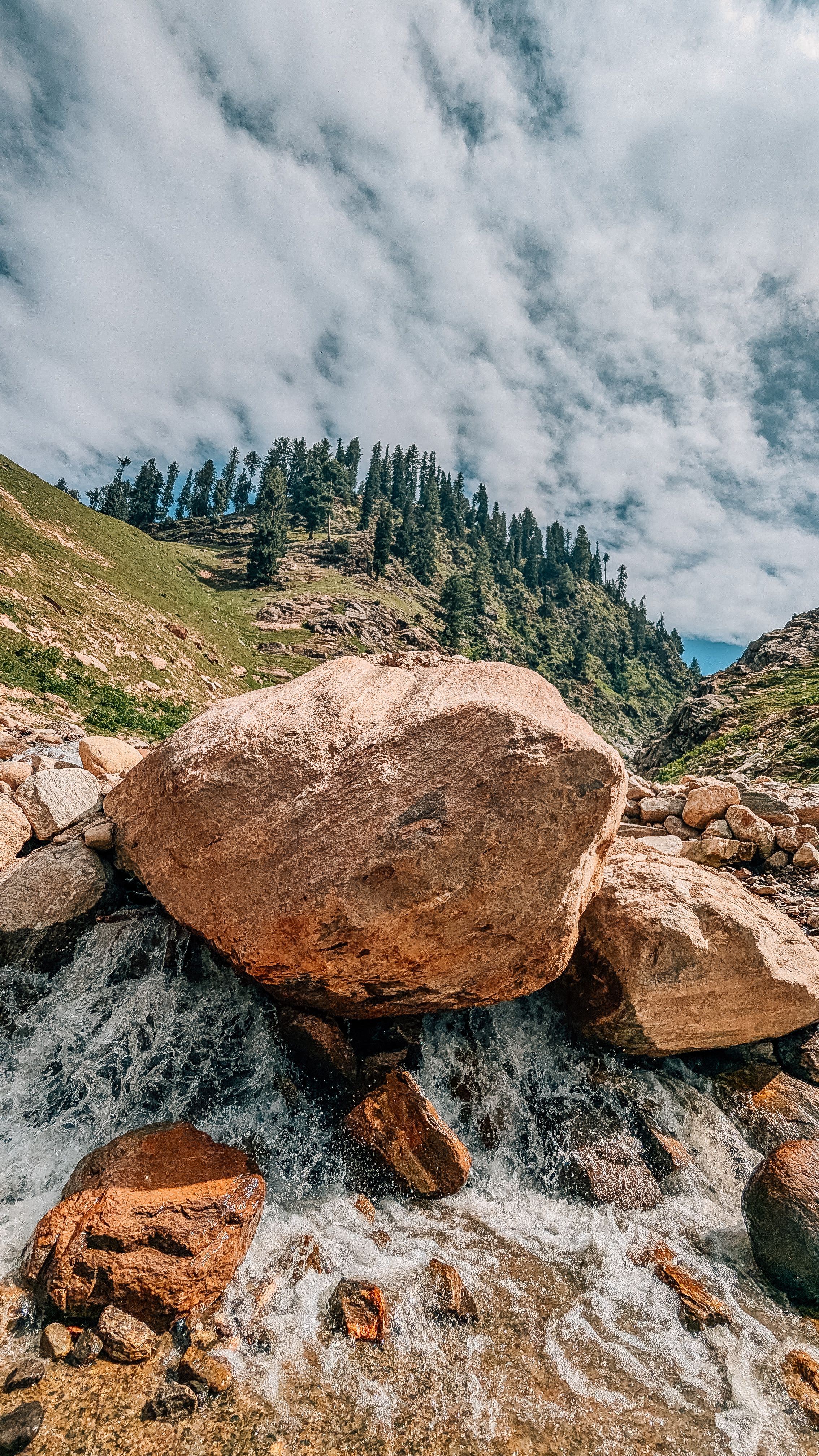 Stunning view of a mountain stream with large boulders, surrounded by lush forest and dramatic sky.