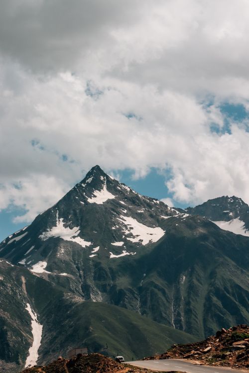 Free A breathtaking view of a snow-capped mountain peak surrounded by clouds and lush greenery. Ideal for nature and travel enthusiasts. Stock Photo