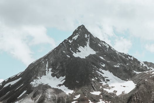 Stunning view of a rugged, snow-dotted mountain peak beneath a cloudy sky.