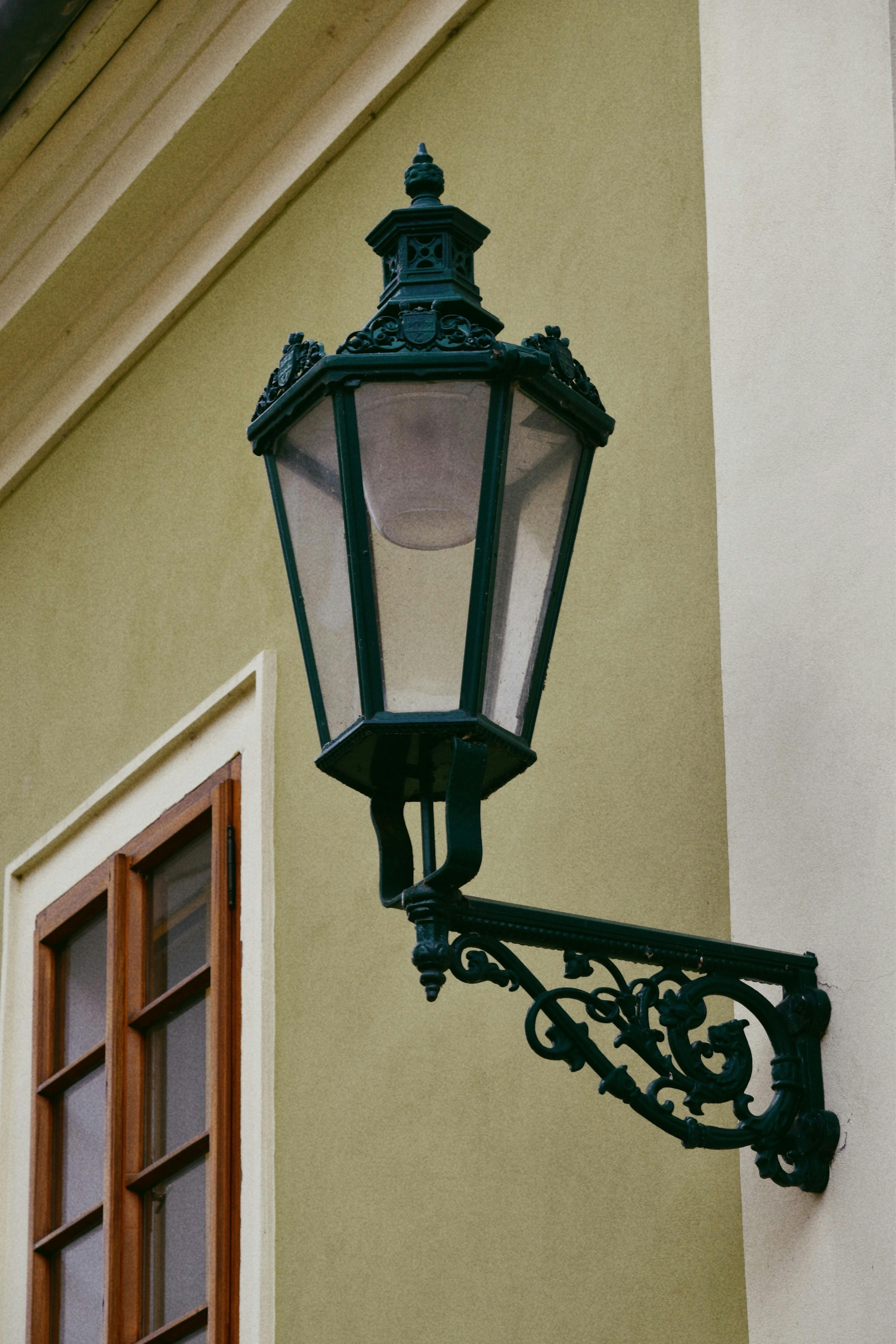 Elegant vintage iron lantern on the side of a classic building with a wooden window.
