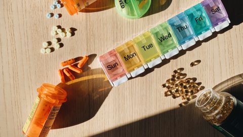Colorful pill organizer with medication bottles and tablets on a wooden surface.
