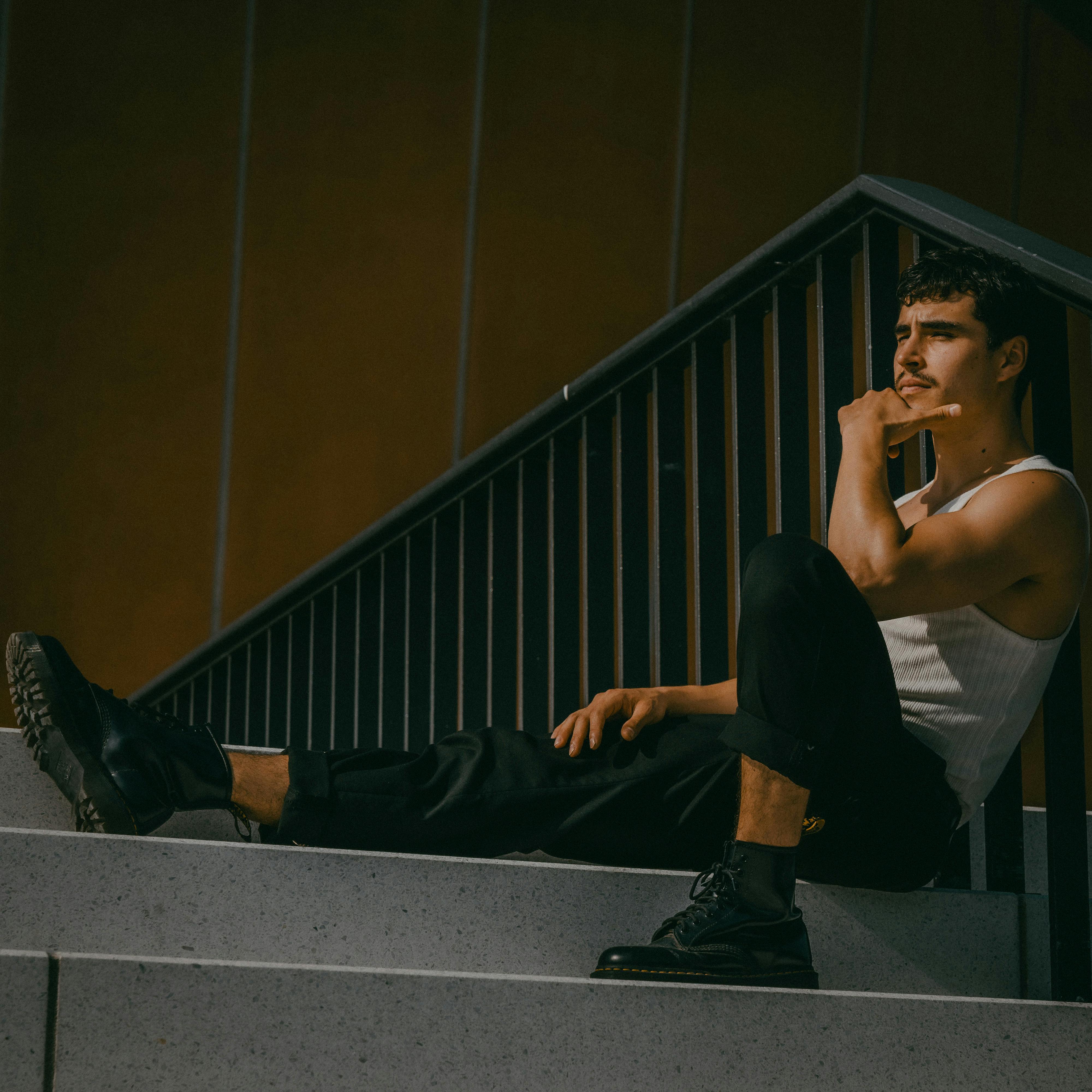 Fashionable young man in Berlin, sitting on stairs, sunlit urban setting.