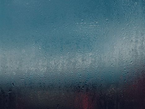 Dramatic close-up of raindrops on a window, showcasing a textured, moody, and cool-toned atmosphere.