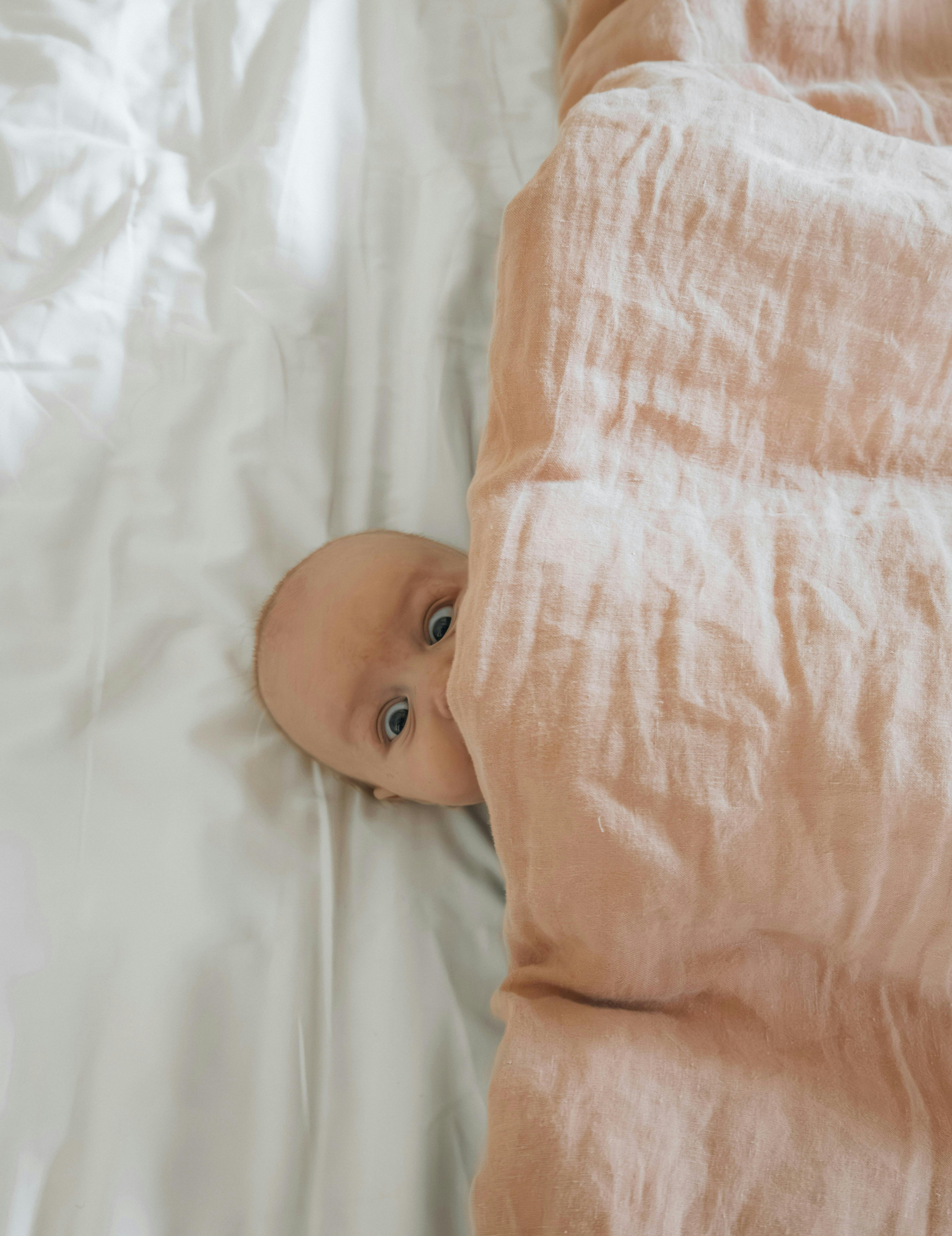 a baby peeks out from under a blanket