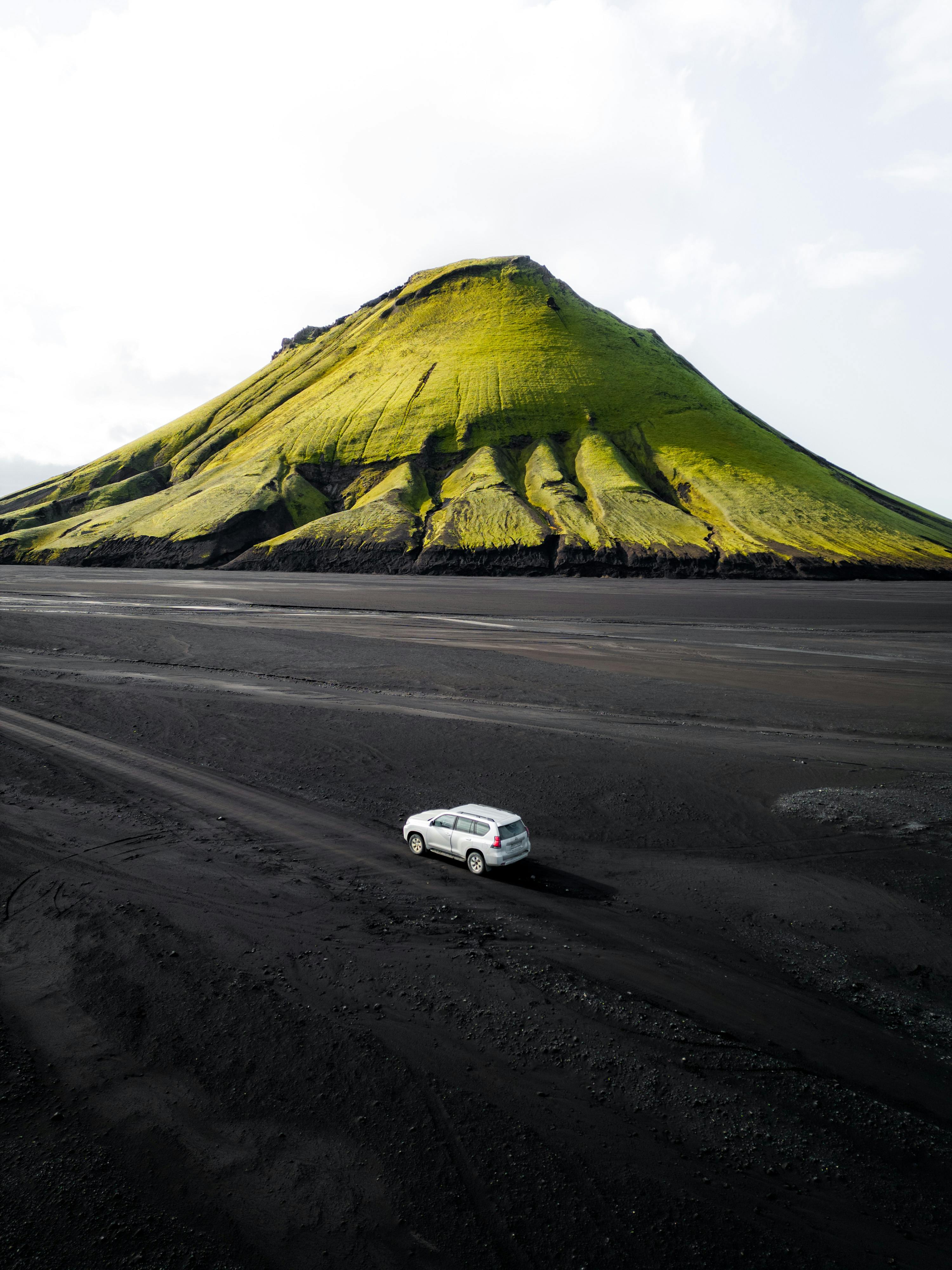 A stunning view of Maelifell volcano with a car in front, showcasing Iceland's rugged beauty.