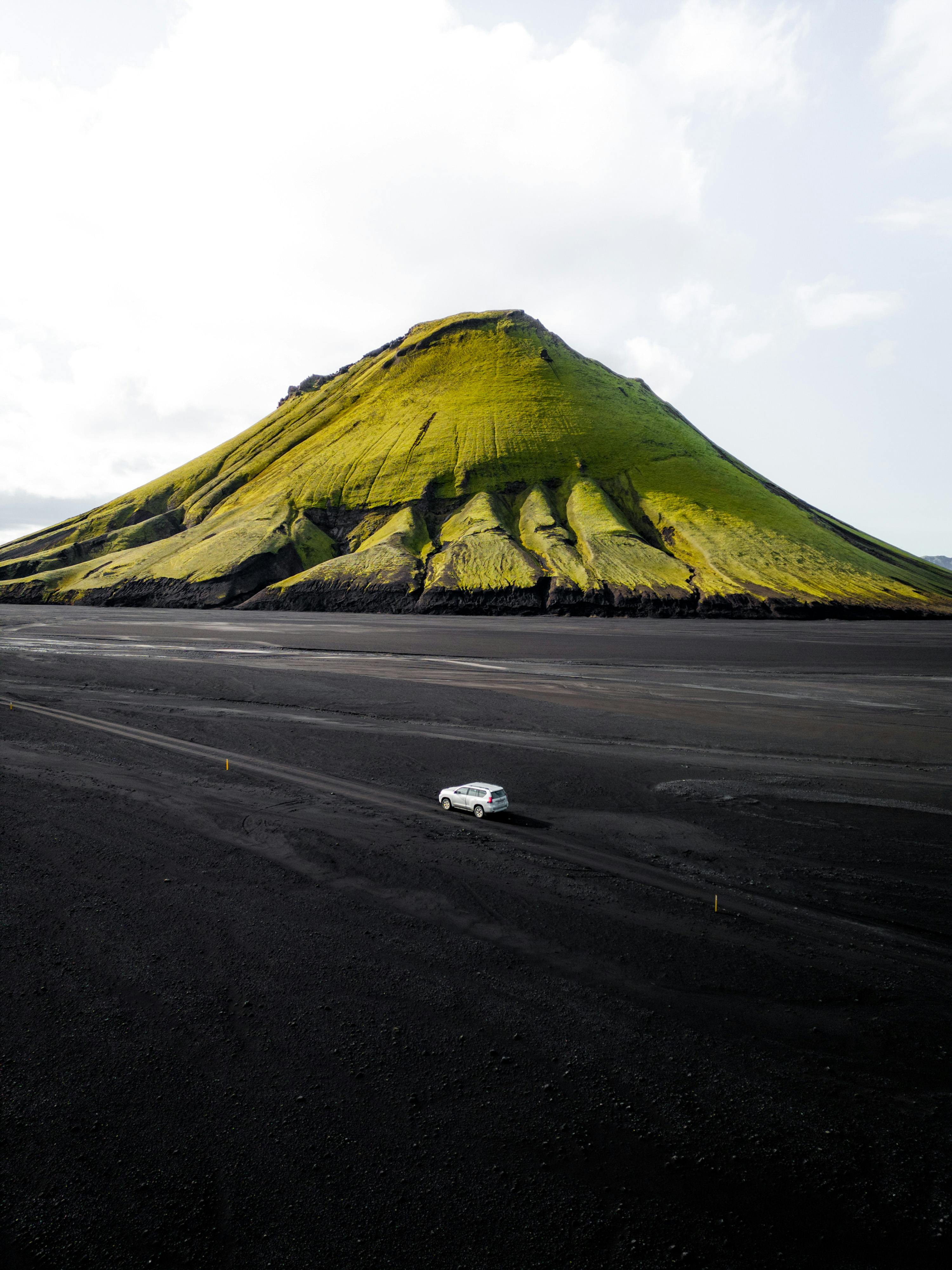 Drone captures Maelifell Volcano in Iceland with an SUV on black sands. Perfect travel and adventure scene.
