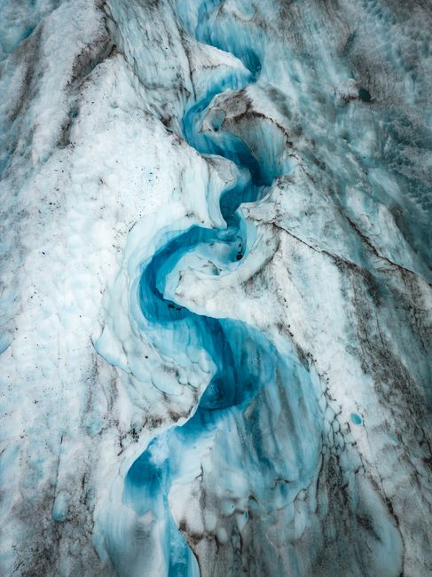 Stunning aerial shot of a vibrant blue stream winding through a glacier in Alaska.