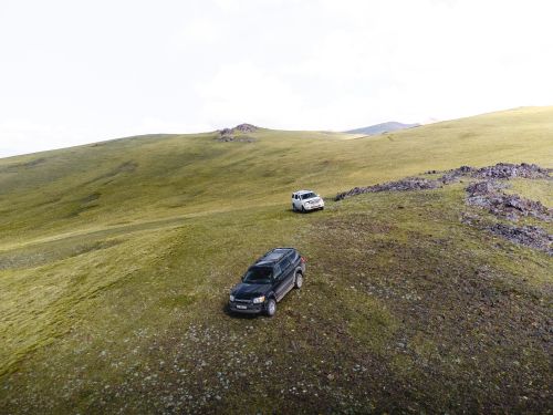 Free Explore the rugged beauty of Kyrgyzstan's vast grasslands with off-road vehicles in this scenic mountain view. Stock Photo