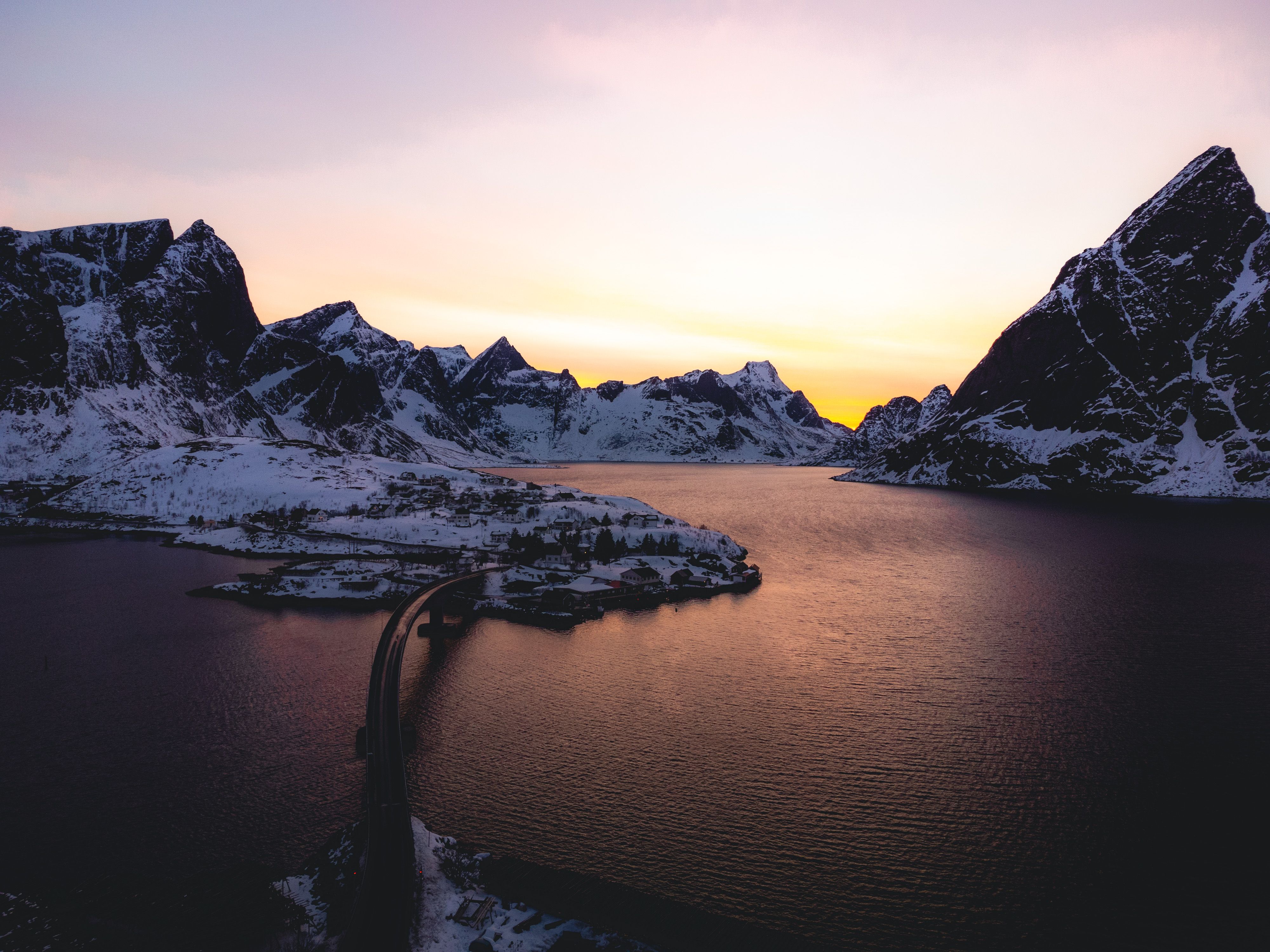 Breathtaking view of snow-covered mountains and tranquil water at sunset in Lofoten, Norway.