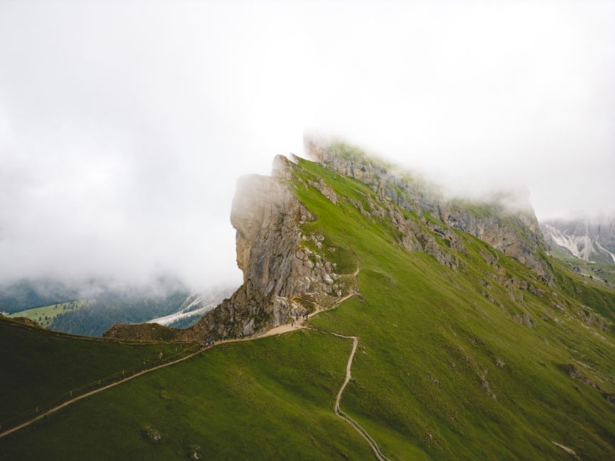 A scenic view of a foggy mountain path in Villnöß, Italy, highlighting lush green landscapes.