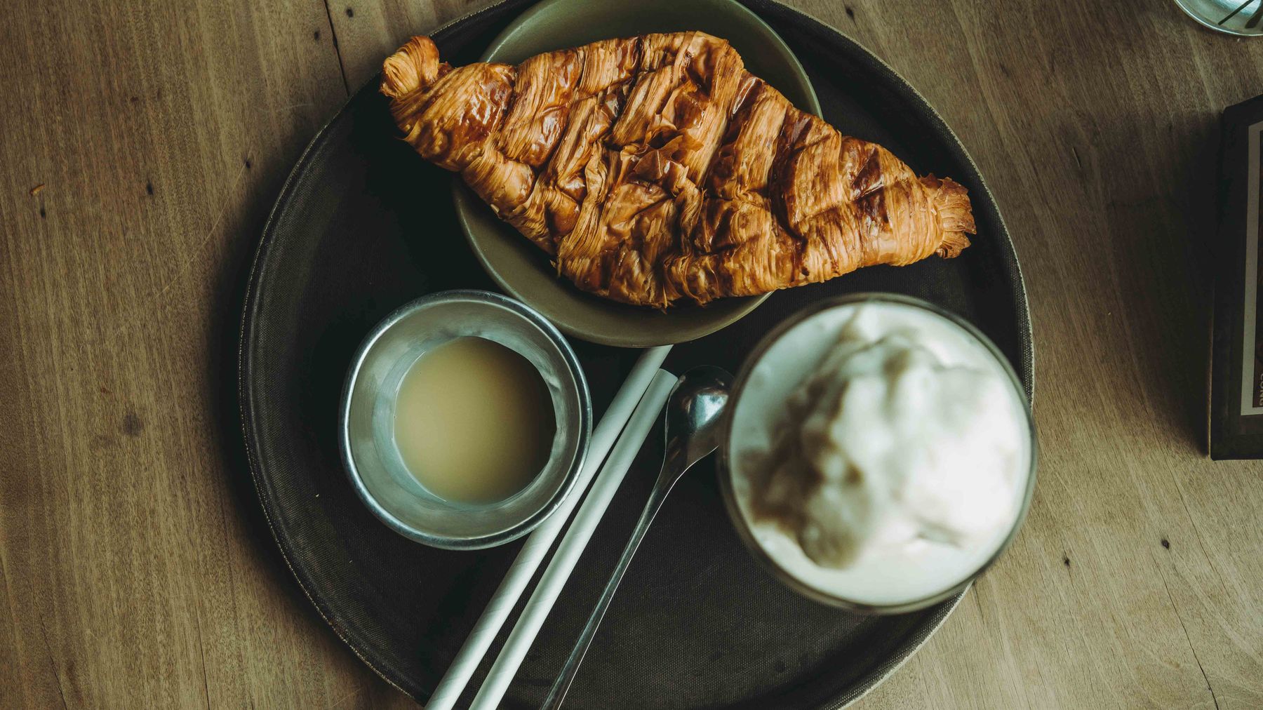 Flat lay of a croissant and coffee with cream on a wooden table, perfect for breakfast themes.