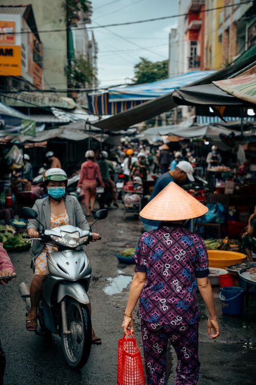 Free Bustling outdoor market in Cần Thơ with people shopping and motorcycles passing. Stock Photo