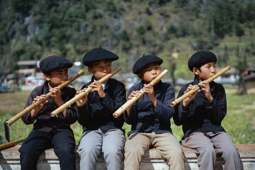Free Four children playing bamboo flutes outdoors in Hà Giang, Vietnam, enjoying musical recreation. Stock Photo