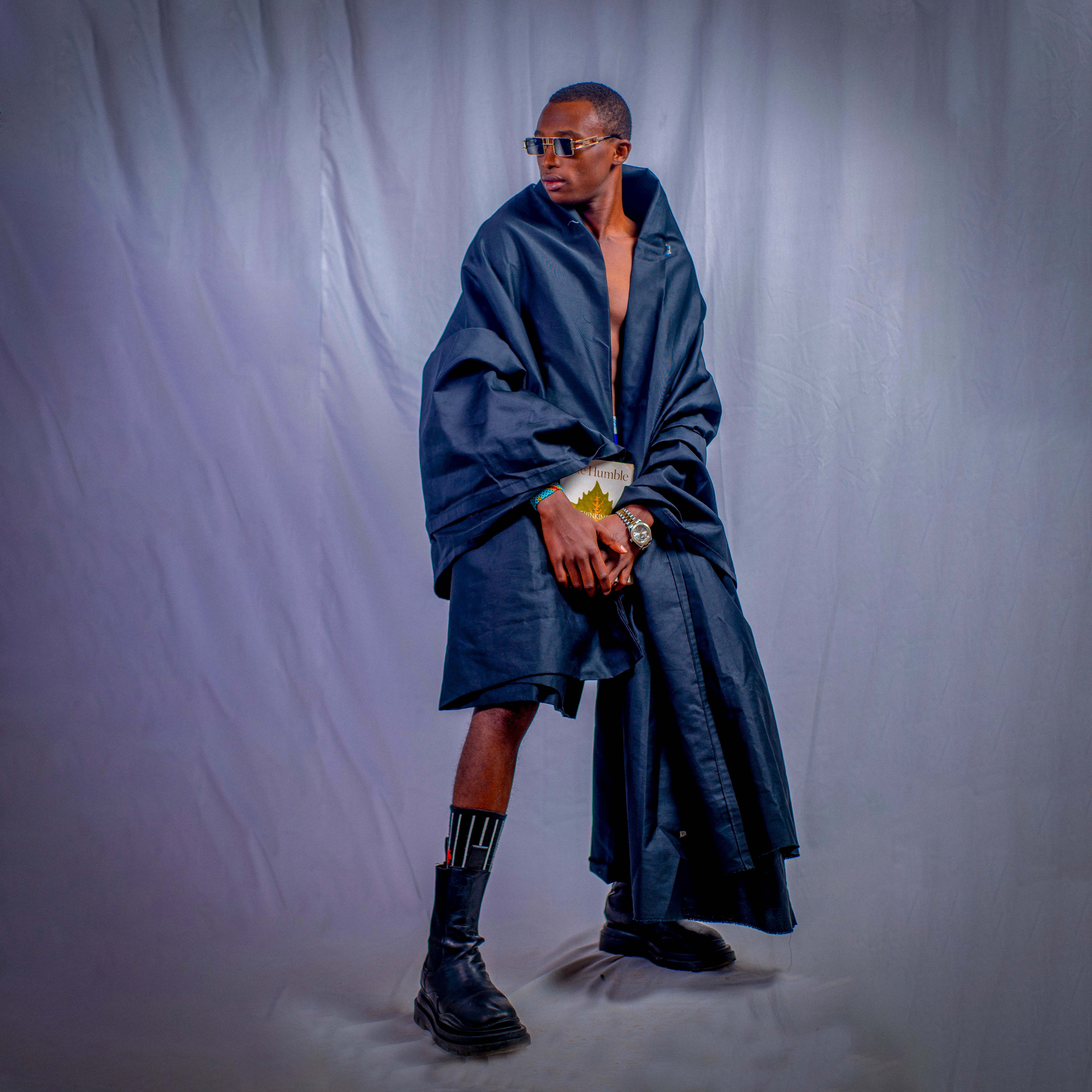 Fashionable portrait of a stylish man in a dramatic studio setting, wearing a dark layered outfit.