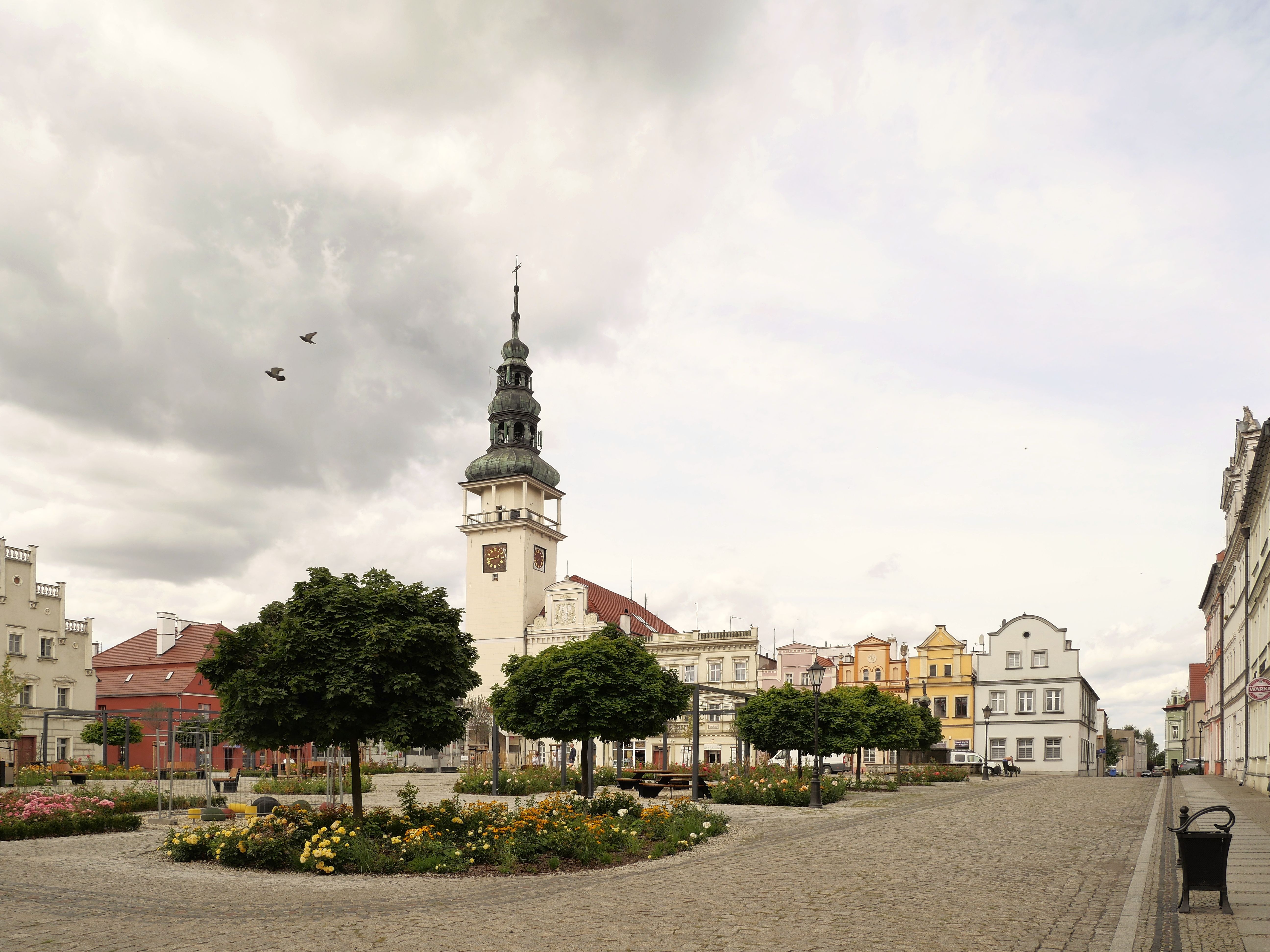 Charming town square in Bytom Odrzański, Poland, showcasing historic architecture under a cloudy sky.