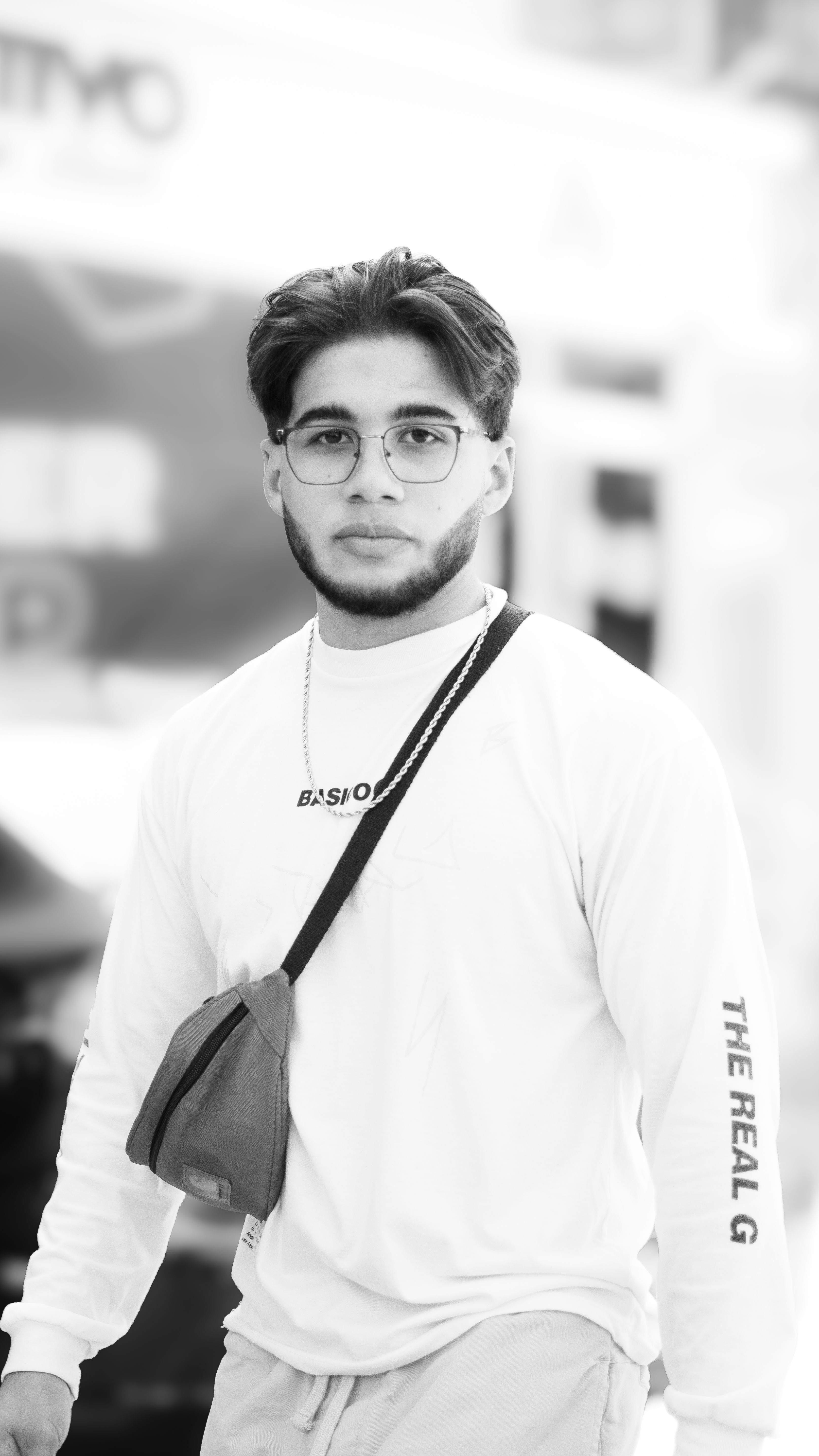 Black and white portrait of a young man wearing eyeglasses and a casual outfit, exuding a serious expression.