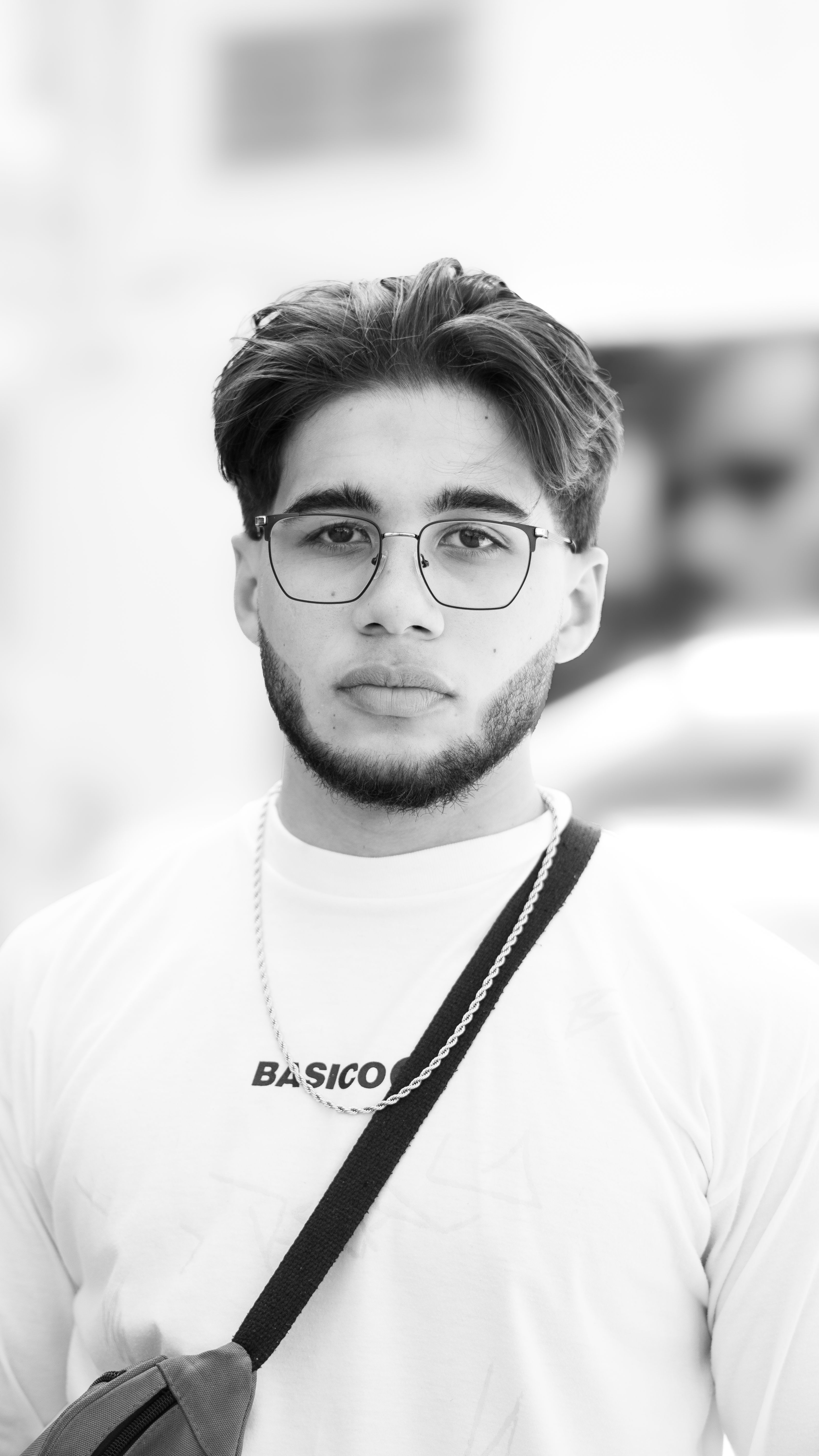 Black and white portrait of a young man wearing glasses and a casual outfit.