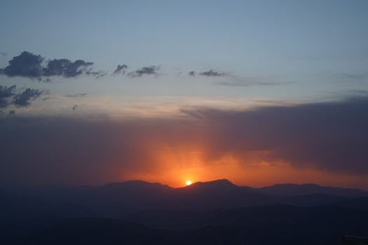 A breathtaking sunset over a mountain range with clouds, captured in a serene landscape.