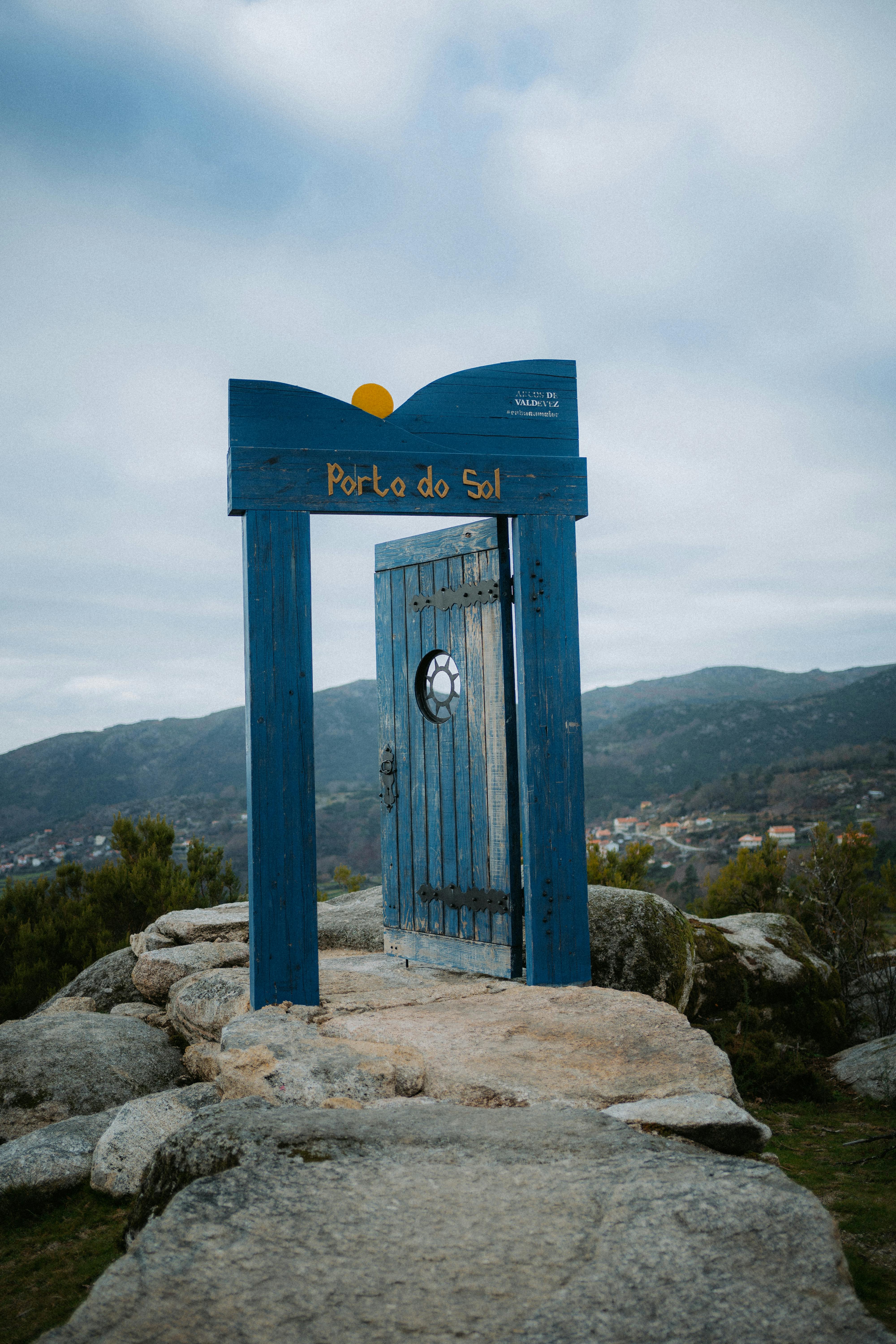 A rustic blue wooden gateway stands on a rocky hillside with mountain views.